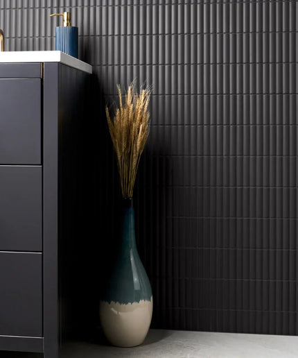 Bathroom with dark gray tiles, a blue vase with dried plants, and a gray cabinet.