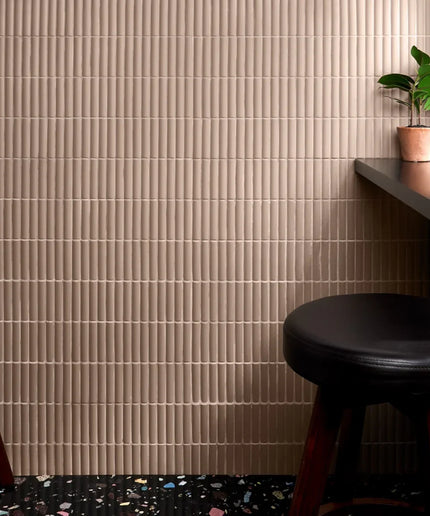 Beige tiled wall with a black stool and small plant in a room.