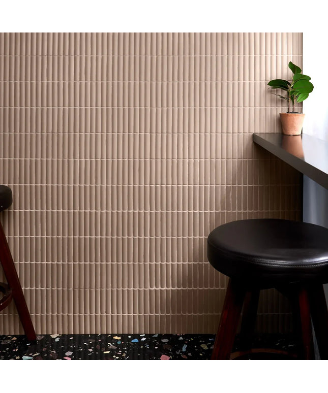 Beige tiled wall with a black stool and small plant in a room.