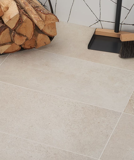 Tile floor with stacked firewood and cleaning tools against a tiled wall.