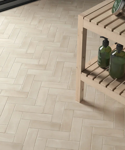 Beige gloss 2x6 tiles in herringbone pattern on floor with wooden shelf and toiletries