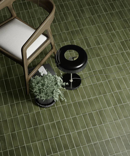 Green matte 2x6 floor tiles with modern wooden chair, black lamp, and potted plant