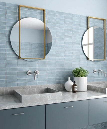Modern bathroom with light blue tile walls, gray countertop, double sinks, and round mirrors