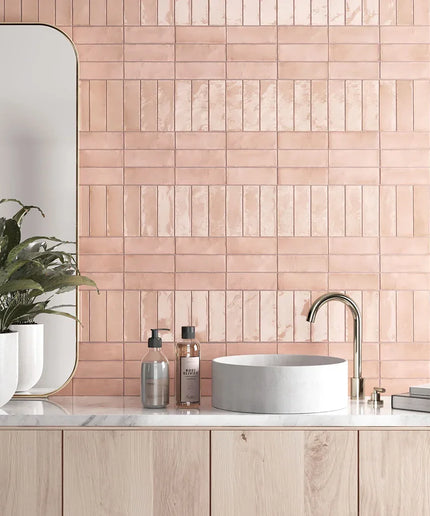 Glossy pink 2x6 subway tiles in a modern bathroom backsplash with round basin and gold faucet