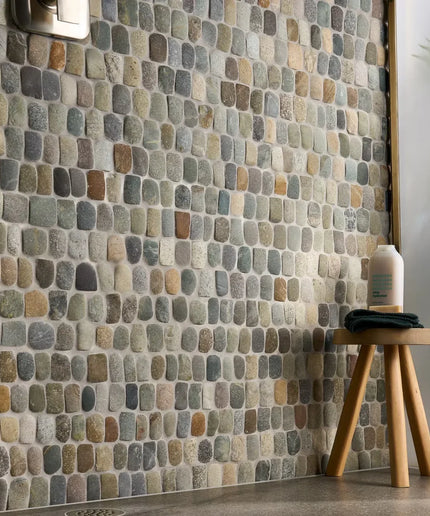 Wall with stone mosaic tiles and a wooden stool with a bottle on it.