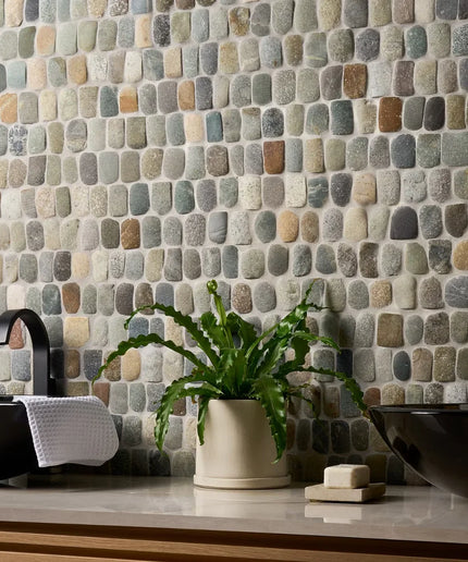 Bathroom with stone mosaic wall, black sinks, and a potted plant.