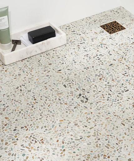 Terrazzo micro floor tiles in a shower with a marble tray, shave gel, and soap bar