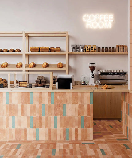 A cozy bakery interior with wooden shelves displaying assorted breads and pastries, a tiled counter in warm peach and teal tones, a coffee grinder, espresso machine, and a glowing 'COFFEE ROOM' neon sign on the wall.