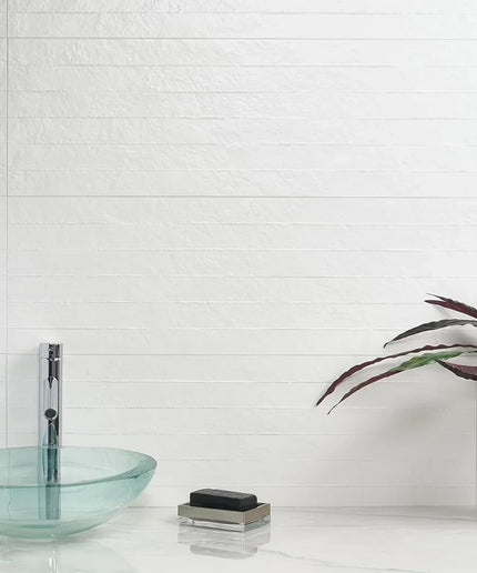 Modern bathroom with glass sink, soap, and plant against a white tiled wall.