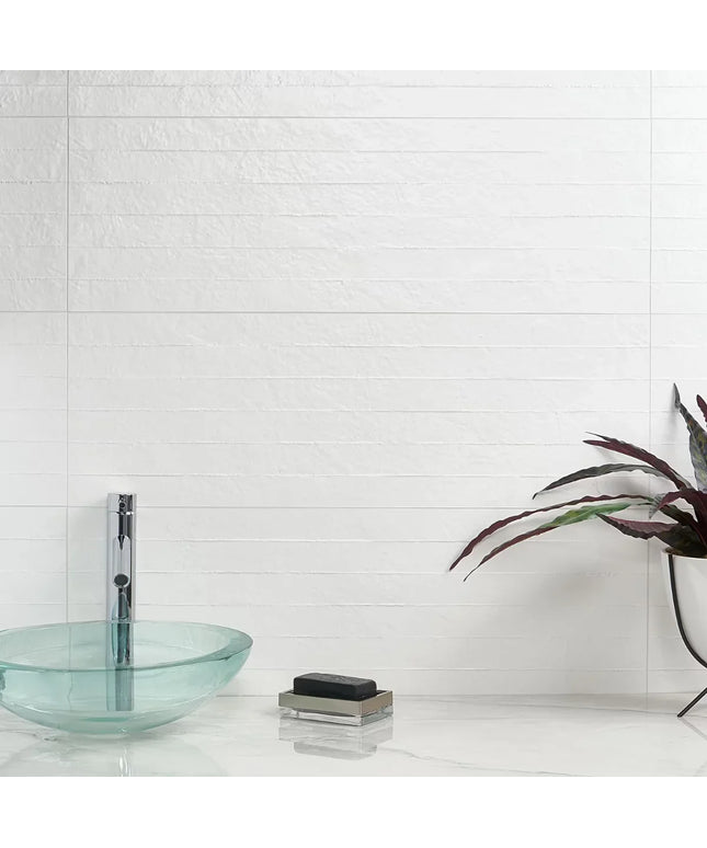 Modern bathroom with glass sink, soap, and plant against a white tiled wall.