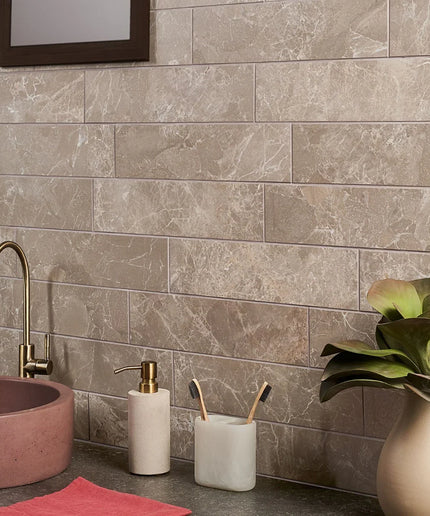 Beige marble-look rectangular wall tiles in a modern bathroom with gold faucet and decor