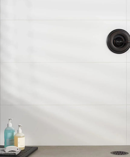 Bathroom sink area with white tiled wall, black drain, and two bottles on a tray.