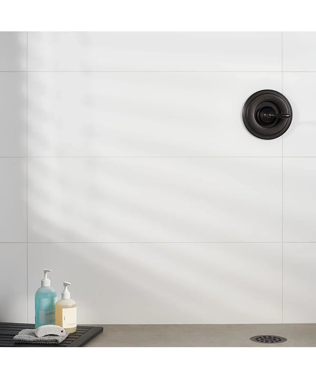 Bathroom sink area with white tiled wall, black drain, and two bottles on a tray.