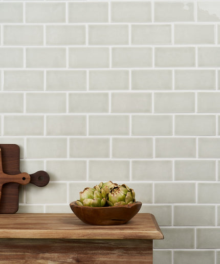 Wooden cutting board and bowl with artichokes against a tiled wall.