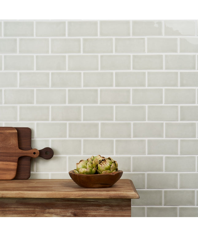 Wooden cutting board and bowl with artichokes against a tiled wall.