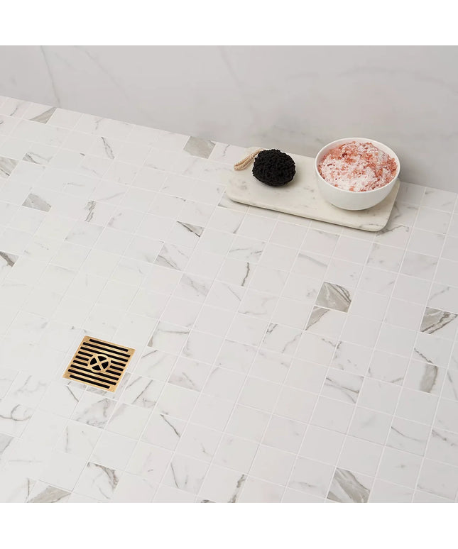 White marble-look mosaic shower floor tiles with gold square drain and bath accessories.