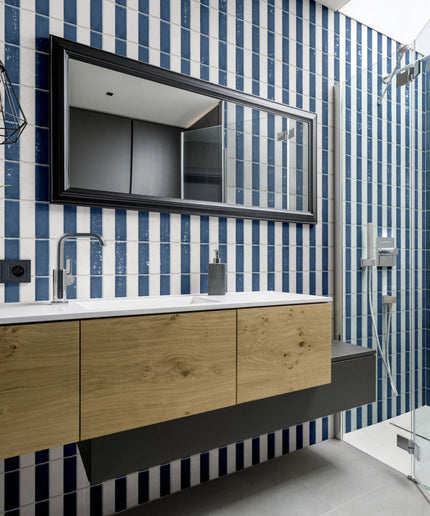 Modern bathroom with blue and white vertical wall tiles, wood vanity, and glass shower