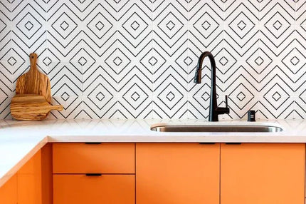 Modern kitchen backsplash with white tiles and black geometric lines, under white countertop and orange cabinets