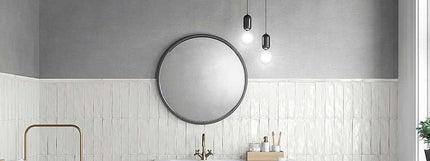 Round mirror on a gray wall with white tiled walls and a sink.